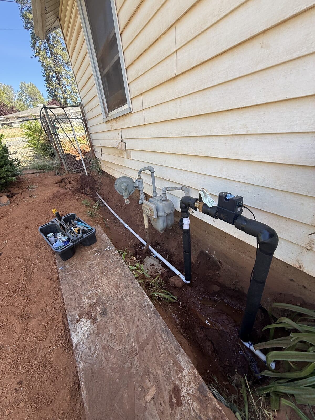 Exterior trench running alongside a home with new valves and fittings installed